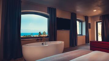 Camera d'albergo moderna con una vasca da bagno ampia, un letto, una TV a parete e vista mare.