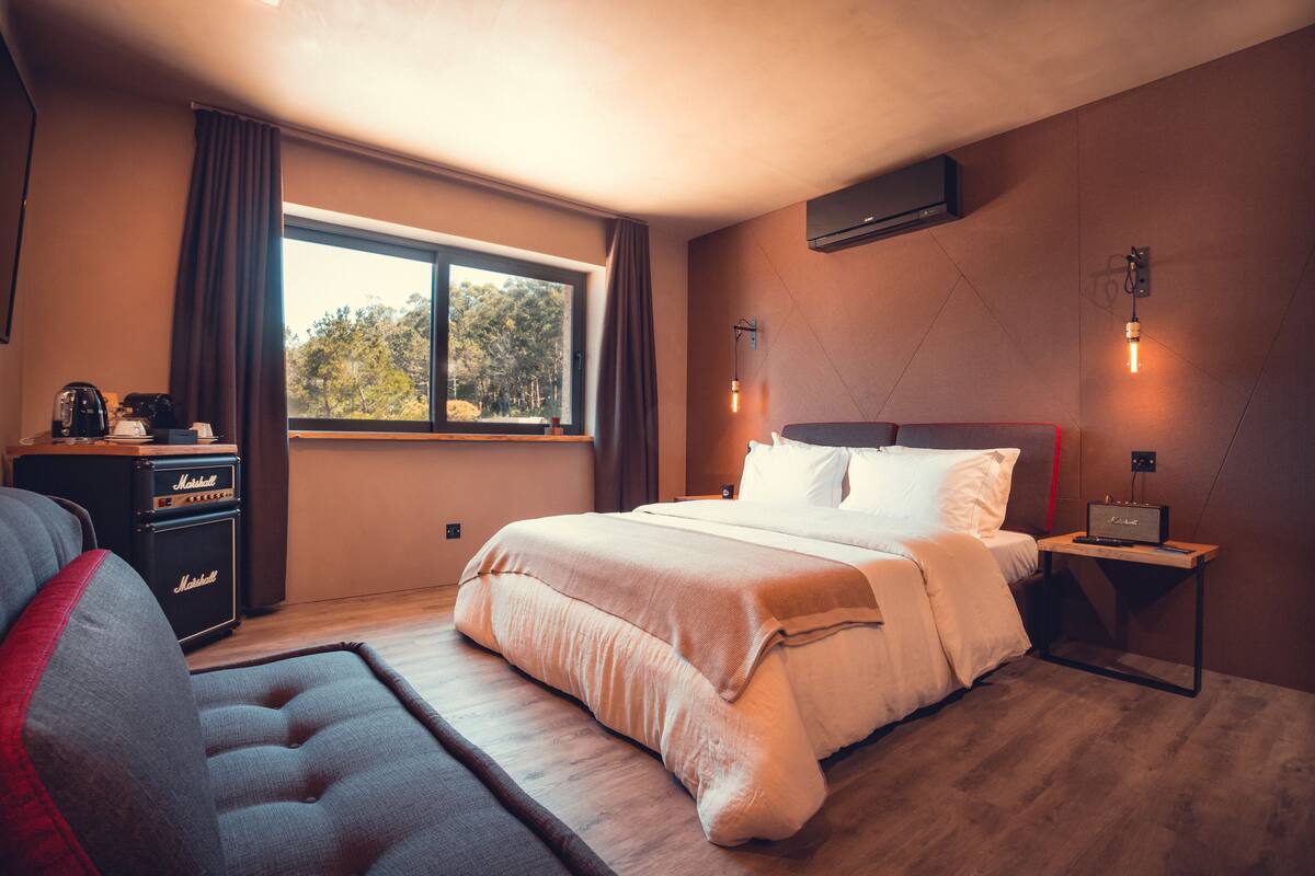 A modern bedroom with a large bed, a desk with a computer, and a window with curtains.