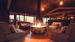 Un rincón de descanso acogedor con una chimenea central, mobiliario de madera y vistas al exterior.