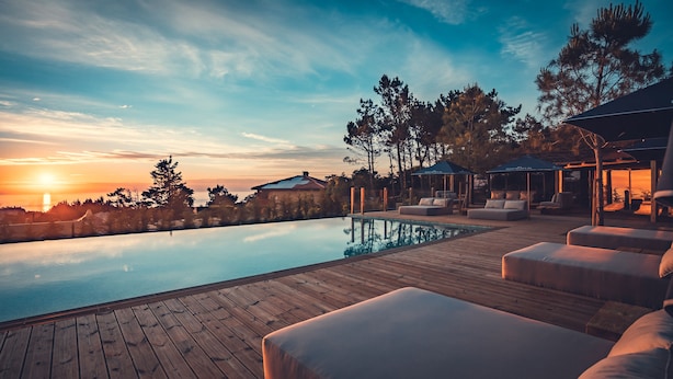 An infinity pool with wooden deck seating, a sunset view, and outdoor umbrellas. - Charm Nature (Sintra)