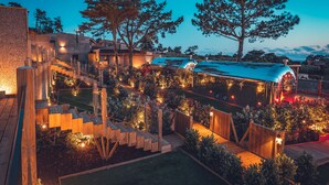 A well-lit outdoor area with a wooden deck, a windmill, and a variety of plants and trees. - Charm Nature (Sintra)