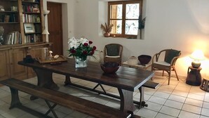 Un área de comedor con una mesa de madera, bancos, una estantería, una ventana con contraventanas decorativas y una lámpara.