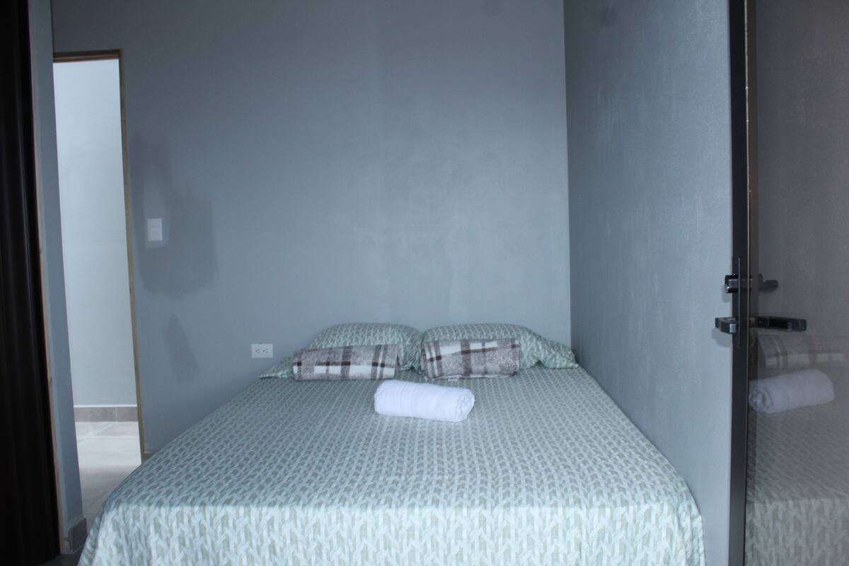 A single bed with a patterned bedspread, two pillows, and a rolled towel on the bed.