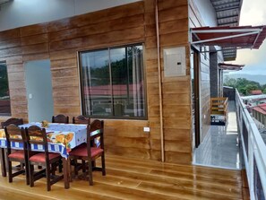A wooden interior with a dining table and chairs, large windows, and a balcony with a railing.