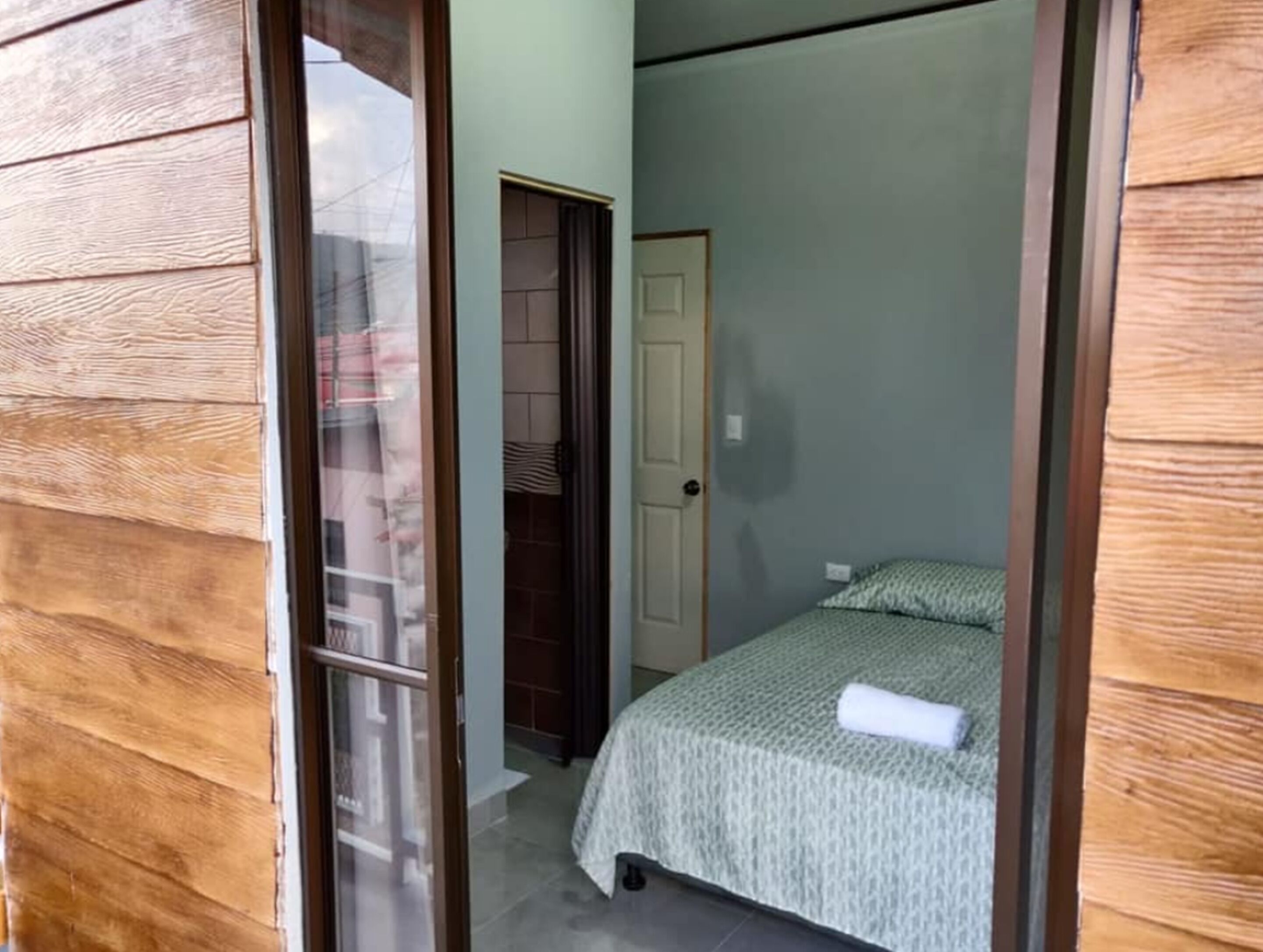 Un dormitorio con cama, una puerta y vistas a través de un ventanal abierto.