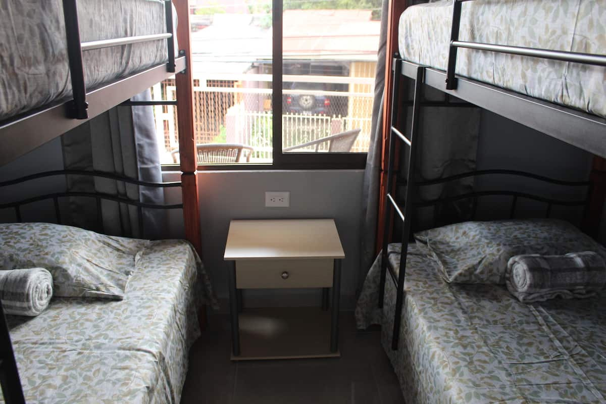 A dormitory room with bunk beds, a small desk, and a window with a view of the outside.