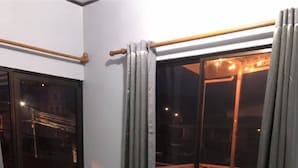 A room with a bed, a window with curtains, and a view of an outdoor area with lights. - Hotel Pacuare Turrialba (Santa Rosa)