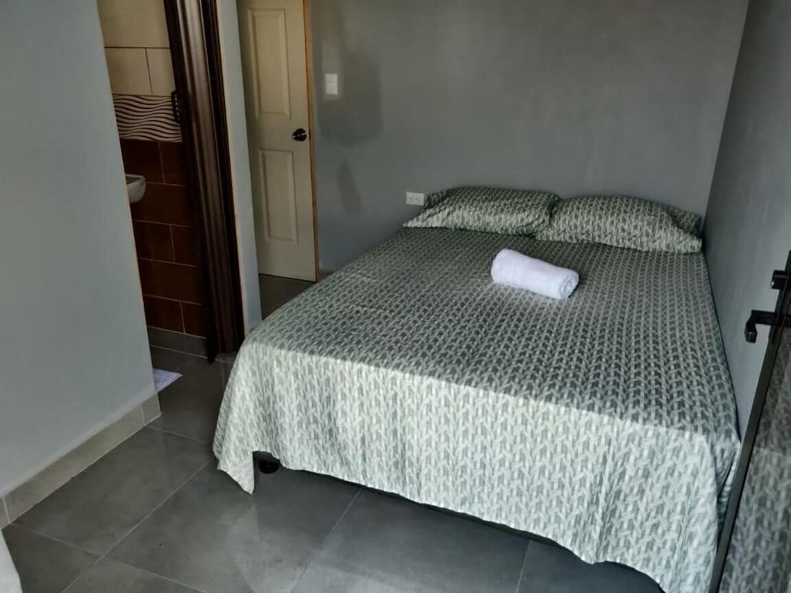 A bedroom with a bed, a door, and a bathroom visible in the background.