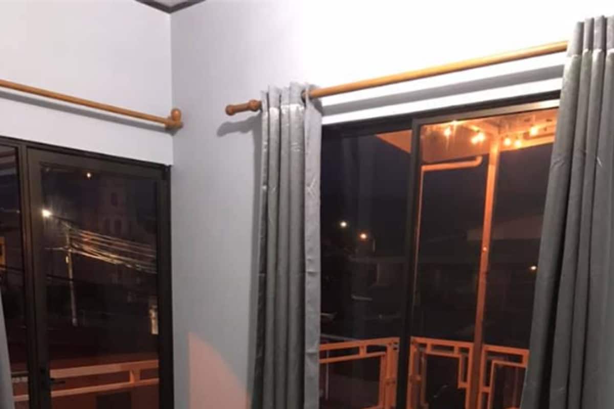 A room with a bed, a window with curtains, and a view of an outdoor balcony.