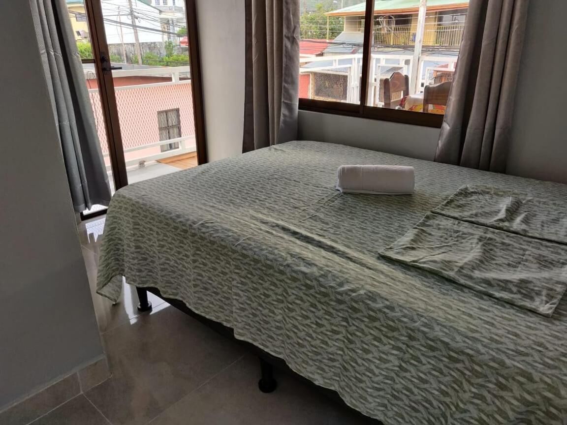 Ein Einzelbett mit einem gemusterten Überwurf, ein gefaltetes Handtuch und ein Fenster mit Vorhängen.