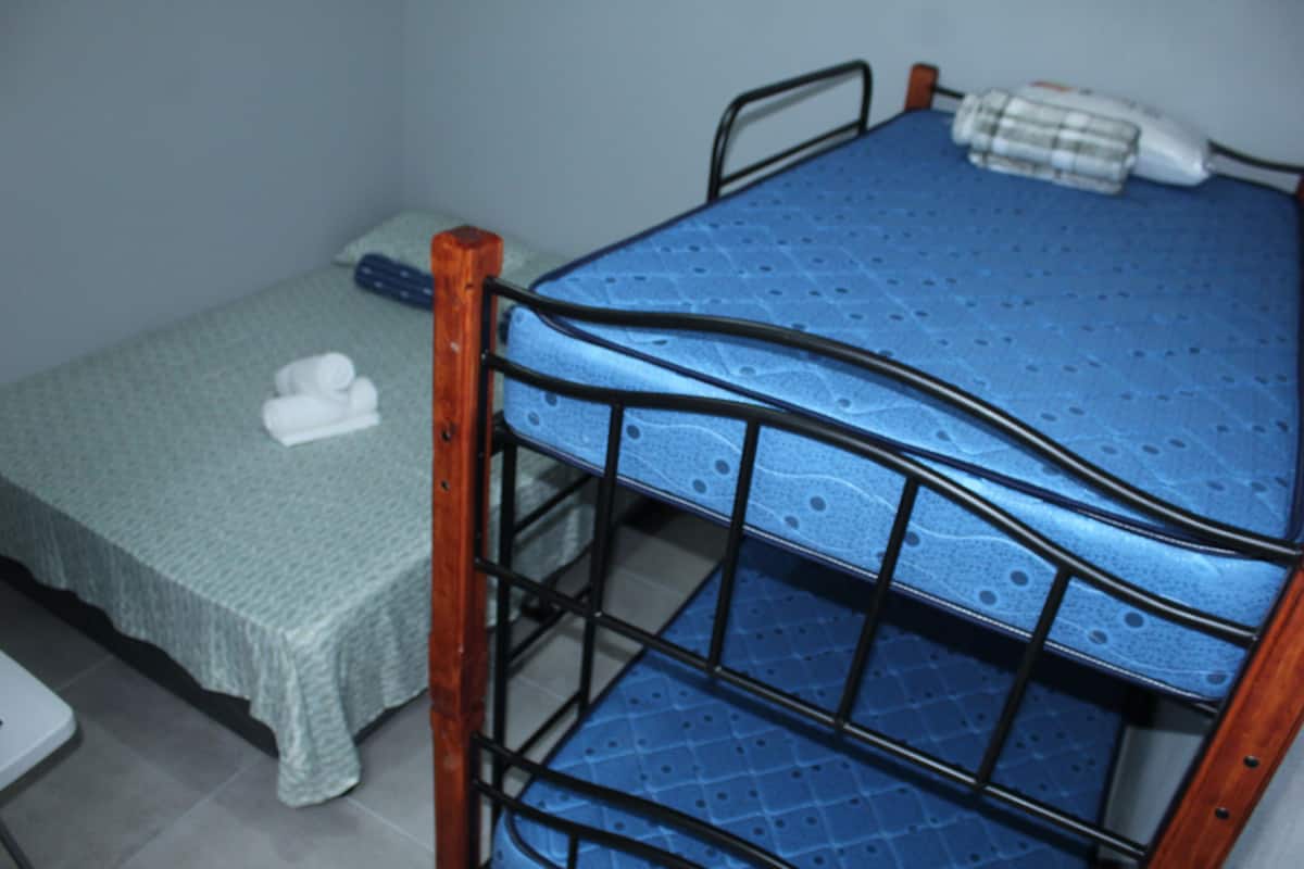 A bunk bed with a blue mattress, a green bedspread, and a white pillow on the lower bed.