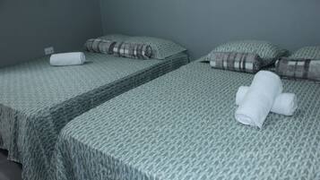 A room with two single beds, each with a patterned bedspread and pillows, and a rolled-up towel on one bed.
