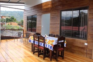 A wooden deck with a table and chairs, large windows, and a view of a hilly landscape.