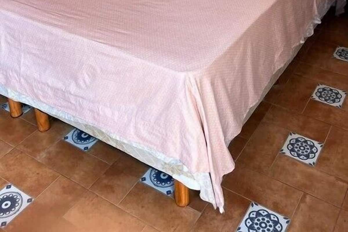 Habitación individual con una colcha rosa, un almohadón blanco y un cabecero de madera.