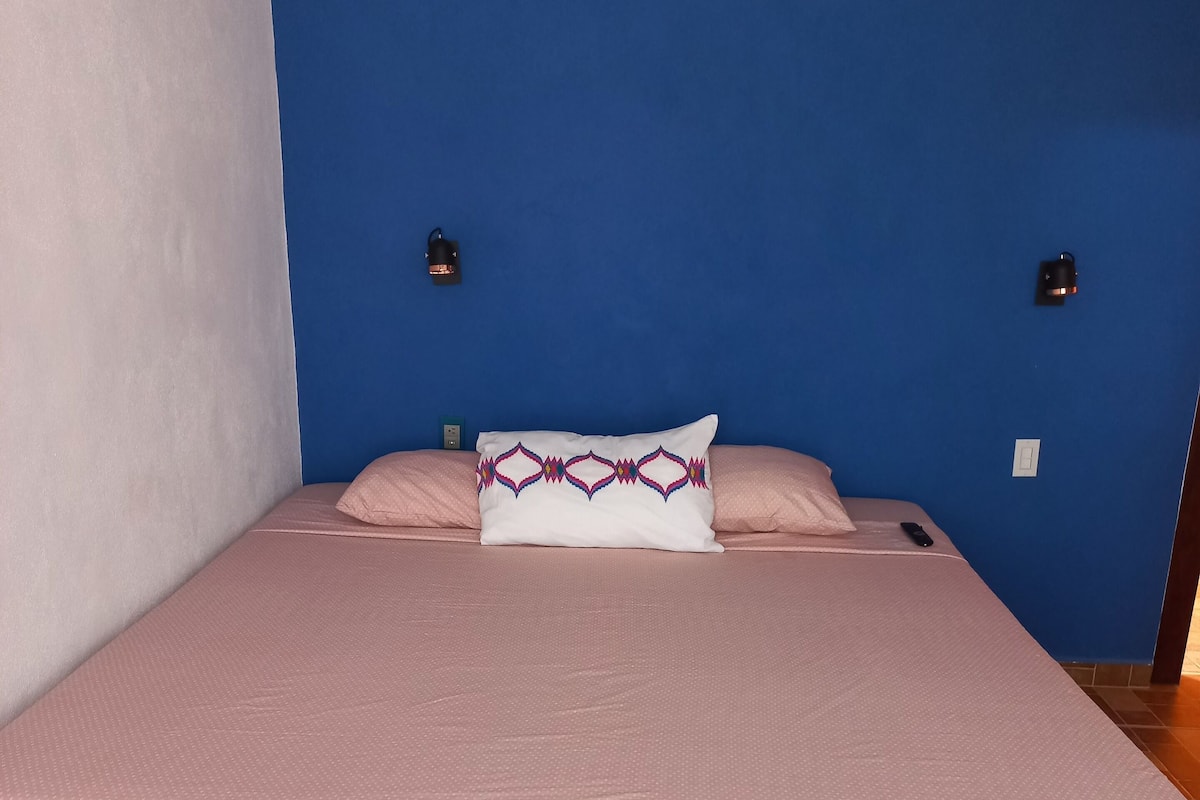 Una cama con una colcha rosa y un cojín decorativo frente a una pared azul.