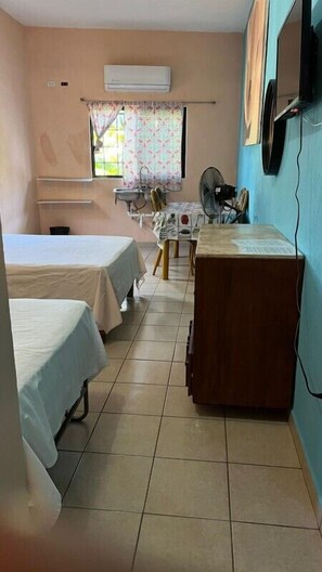 A small, clean room with two beds, a desk, a chair, a fan, and an air conditioning unit. - Familia Sosa Suazo (San José del Cabo)