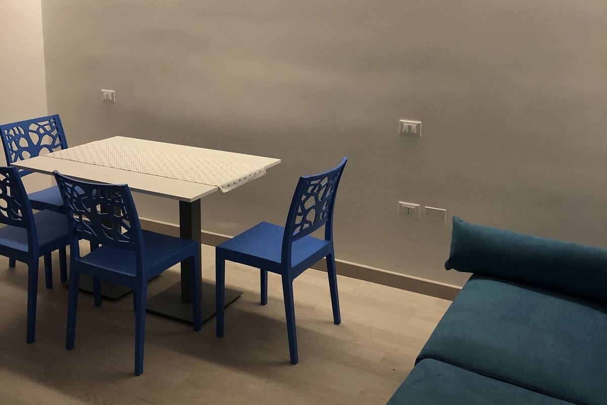 A room with a table and chairs, a sofa, and a wall-mounted light fixture.