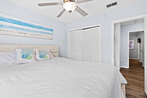 Ein Schlafzimmer mit Bett, Deckenventilator, einem Gemälde und einem Kleiderschrank.