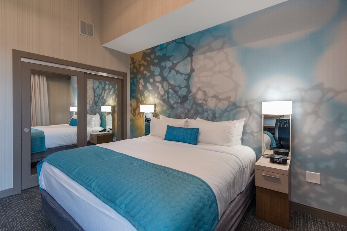 Ein Hotelzimmer mit einem großen Bett, einem Spiegel, einem Nachttisch und einer Wand mit strukturierter Gestaltung.