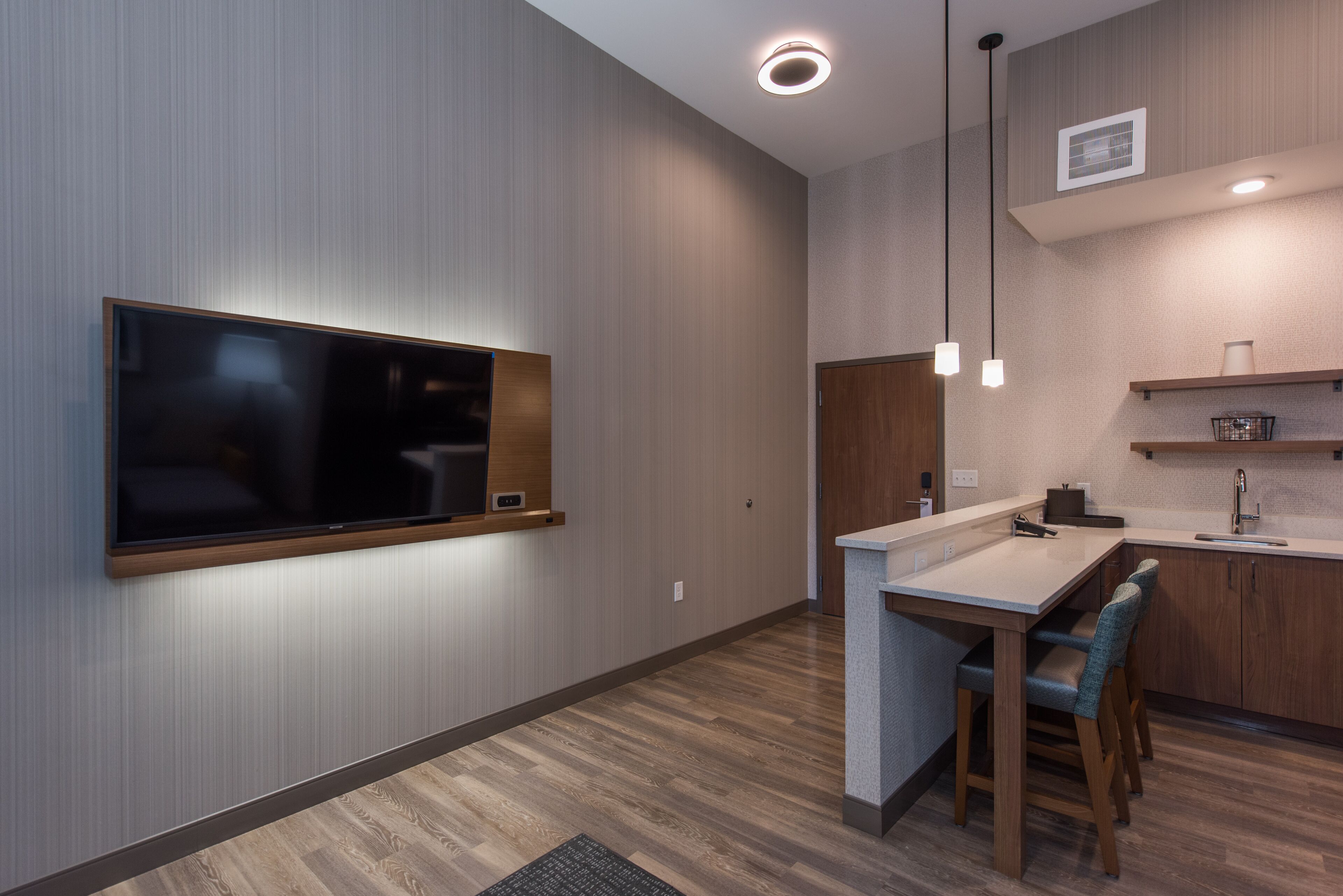 Una cocina moderna con televisión integrada, armarios de madera e iluminación colgante.