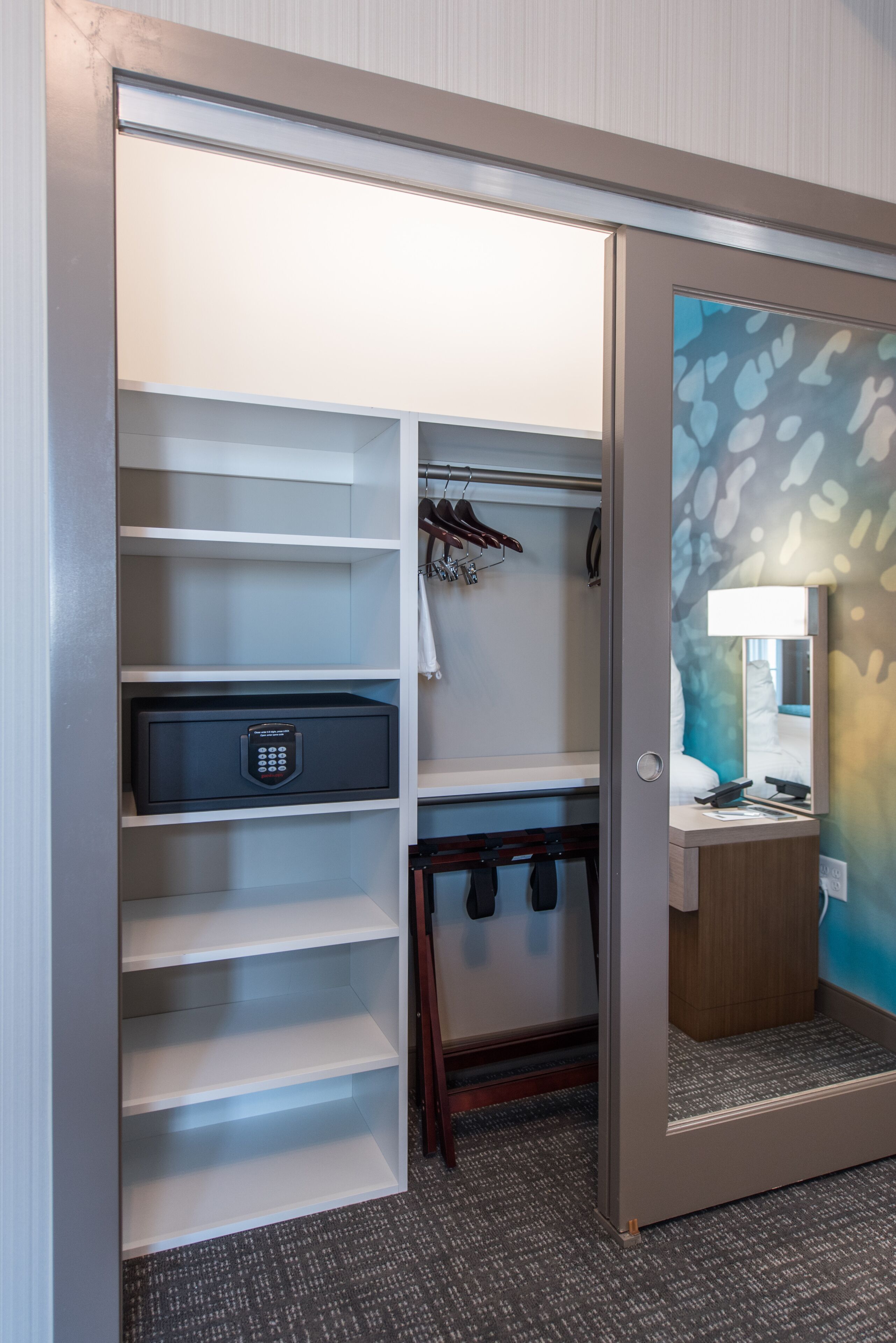 Un placard dans une chambre d’hôtel comprenant à la fois des étagères ouvertes et fermées, une tringle pour suspendre les vêtements et un petit espace bureau avec une lampe et un miroir.