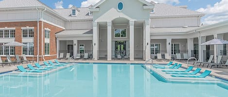 A swimming pool with lounge chairs and a building with a central entrance.
