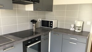 A modern kitchen with grey cabinets, a built-in microwave, a coffee maker, and a stainless steel range hood. - Large T3 loggia in house 500m from the beach (saint cyprien)