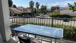 A balcony with a metal table and chairs, overlooking a street with cars and houses. - Large T3 loggia in house 500m from the beach (saint cyprien)