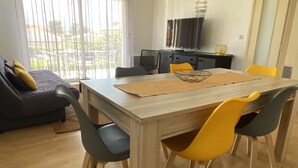 A dining area with a wooden table, yellow chairs, and a black sofa. - Large T3 loggia in house 500m from the beach (saint cyprien)