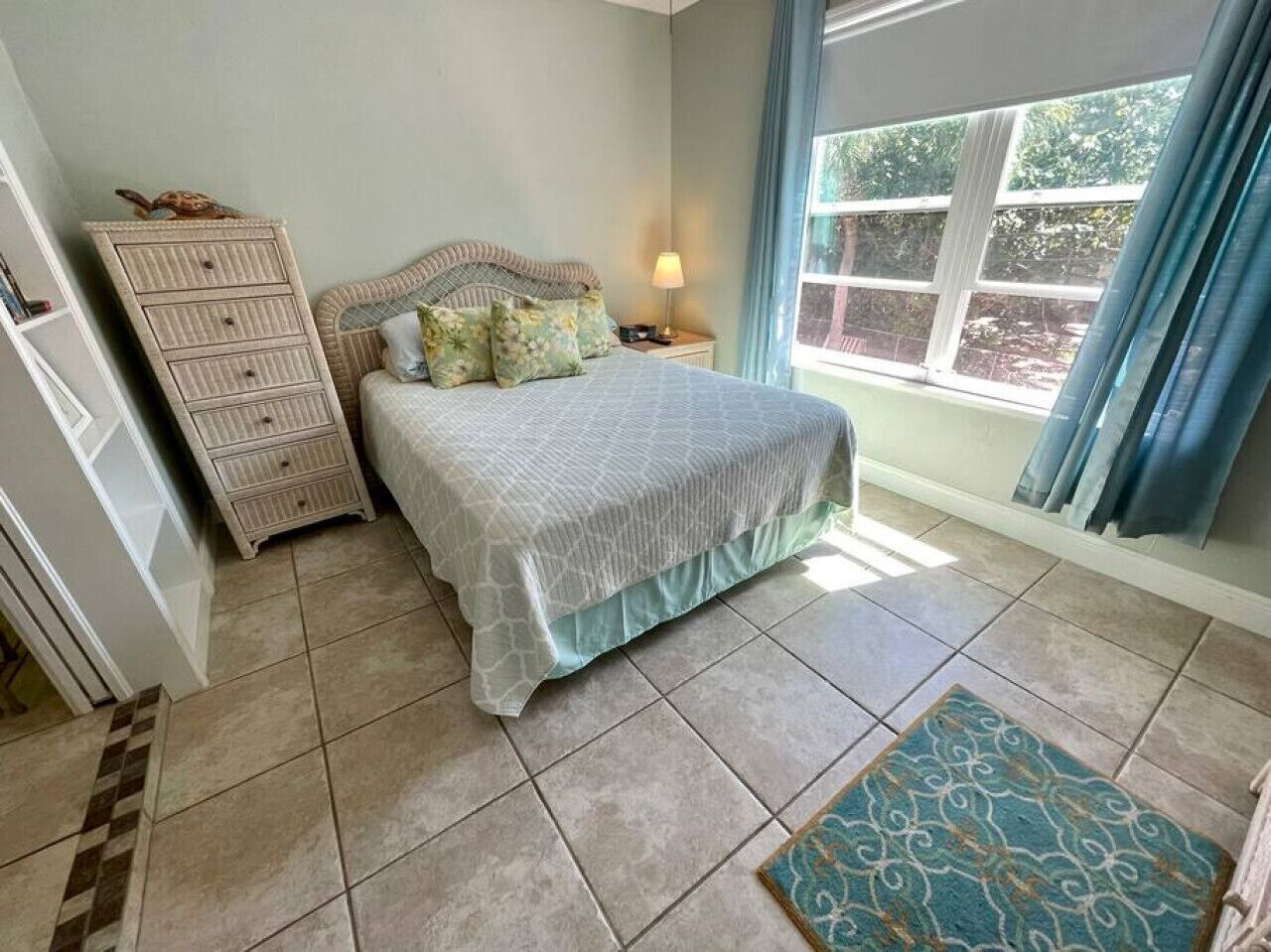 Quarto com cama, mesa de cabeceira, penteadeira e janela com cortinas.