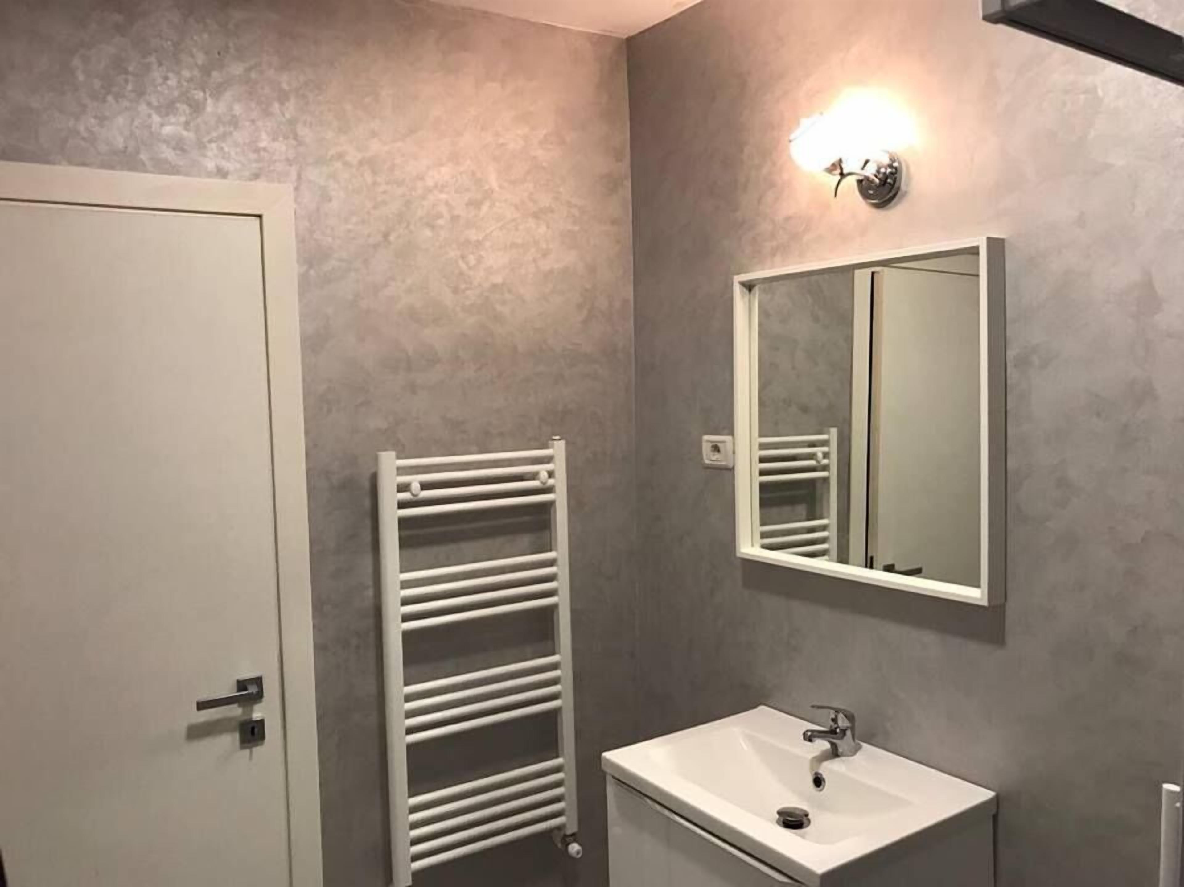A bathroom with a white door, a white towel rack, a white sink, and a mirror with a light above it.