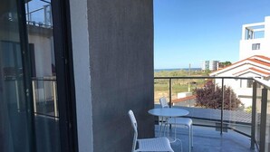 Un balcón con puerta de vidrio, dos sillas blancas y una mesa pequeña.
