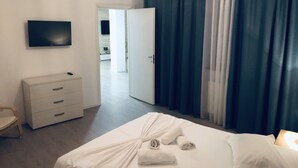 Una habitación de hotel con una cama, televisión, cómoda y una puerta que da a un baño.