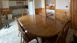 Uma área de refeições com uma mesa e cadeiras de madeira, uma cozinha ao fundo e uma porta de madeira.