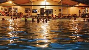 Un espace piscine doté d’une terrasse couverte et d’un bâtiment en arrière-plan.