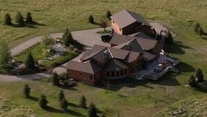 Une grande maison à plusieurs étages, dotée d’une cheminée imposante, entourée d’une pelouse bien entretenue et de plusieurs arbres.