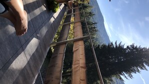 Eine Holzterrasse mit Metallgeländer, ein Holzmast mit einem Glas darauf und Blick auf eine gebirgige Landschaft.