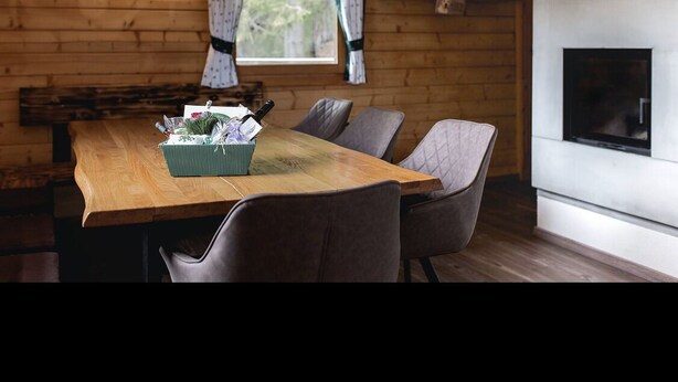 Ein gemütliches Blockhäuschen-Interieur mit einem Holzespeisetisch, zwei Stühlen, einer Pendelleuchte und einem Kamin.