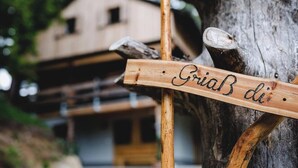Ein Holzschild mit der Aufschrift 'GriaB di' an einem Baum befestigt.