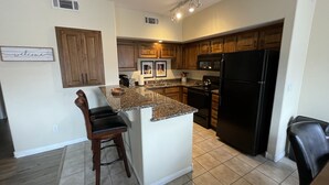 A kitchen with wooden cabinets, a black refrigerator, a granite countertop, and a bar stool.