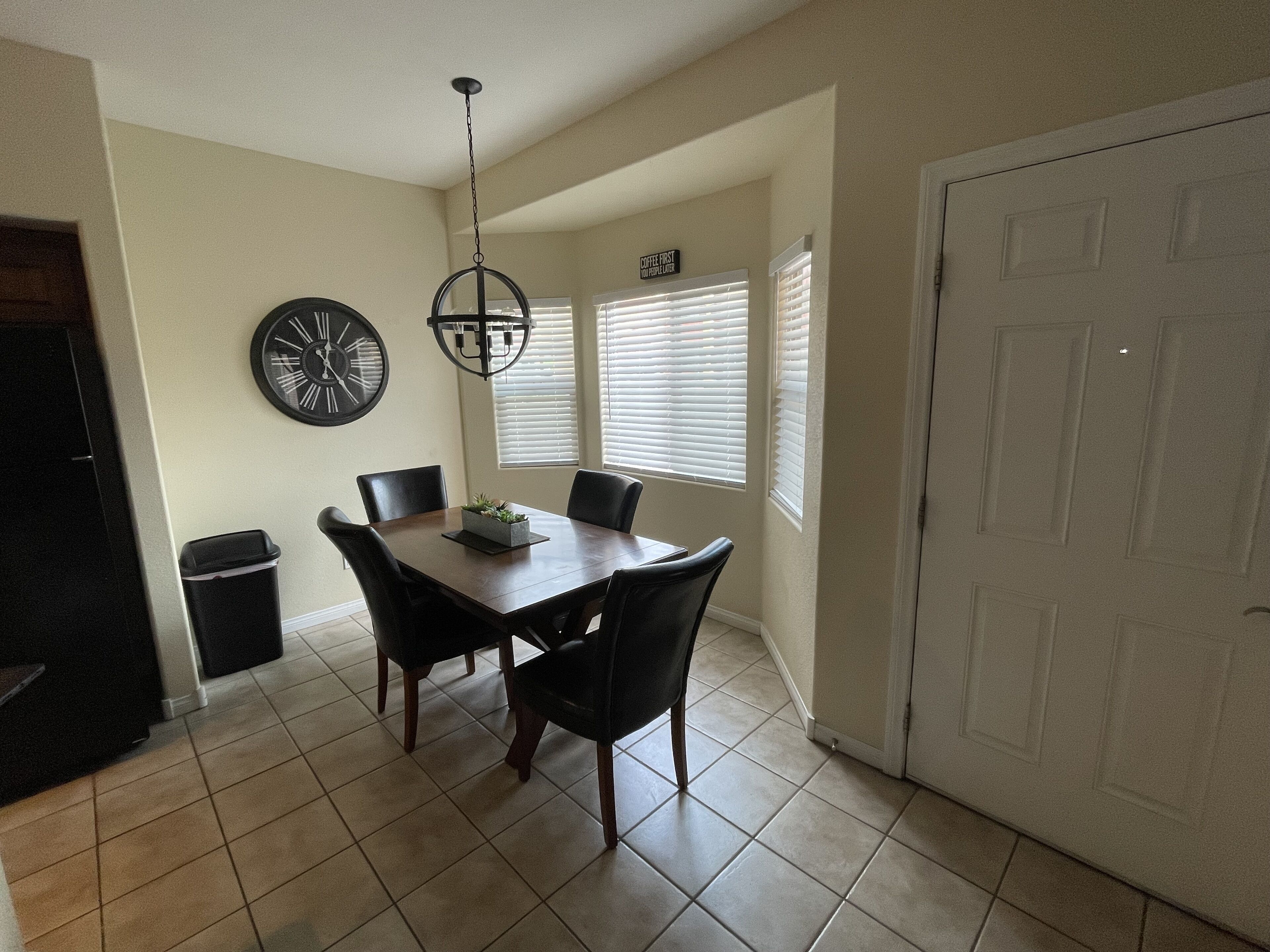 Un comedor con una mesa rectangular, cuatro sillas, un reloj y un cubo de basura.