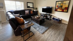 A living room with a black leather sofa, a coffee table, a TV, and a ceiling fan.
