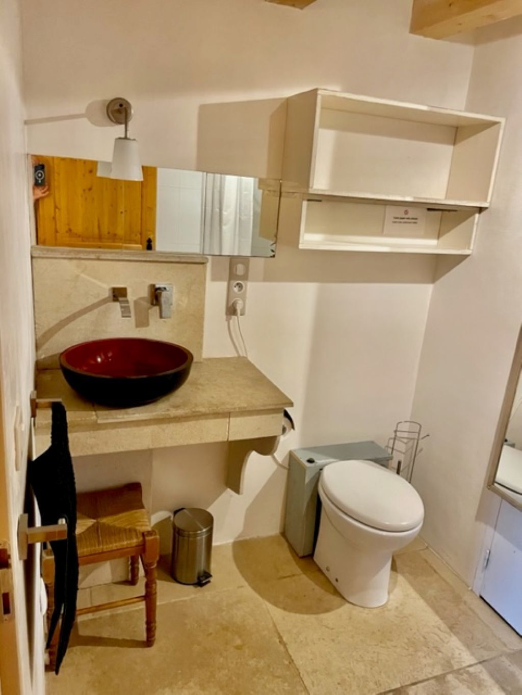 Ein Badezimmer mit einem roten Waschbecken, einer weißen Toilette, einer kleinen Mülltonne und einem hölzernen Stuhl.