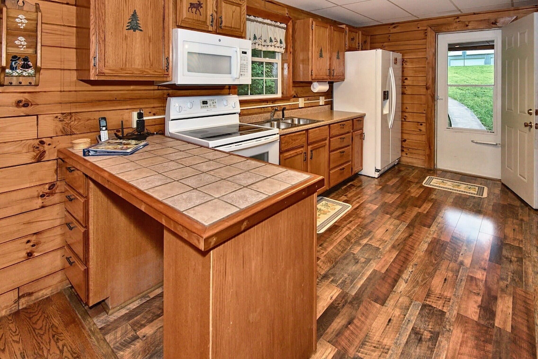 A kitchen with wooden cabinets, a microwave, stove, refrigerator, and a window with a view of the outdoors.