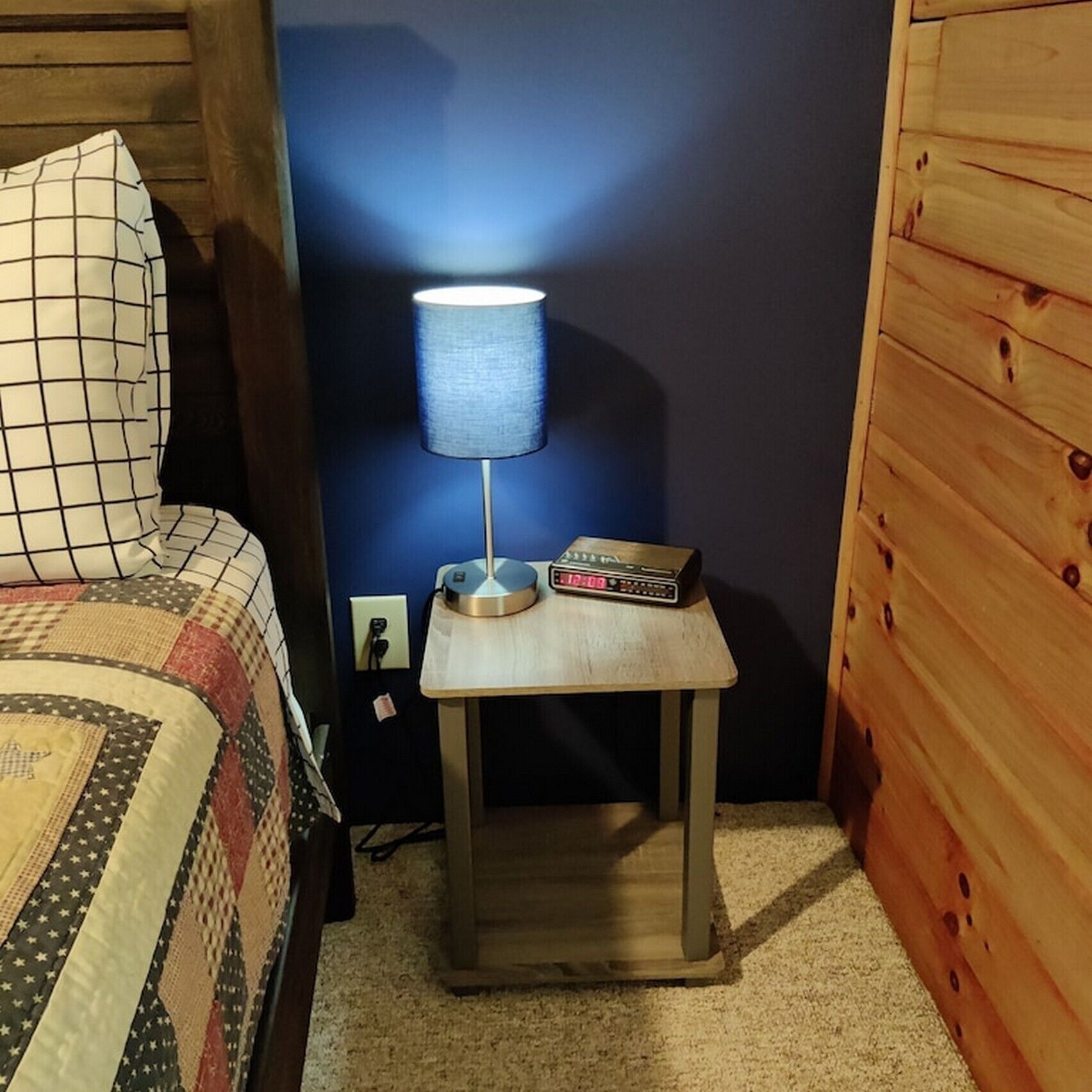 Ein kleines Zimmer aus Holz mit einem Bett, einem Nachttisch mit Lampe und einer Uhr.