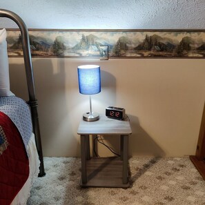 A bedroom with a bed, a nightstand with a lamp and a digital clock, and a painting on the wall. - Wildflower Cabin in Hocking Hills | Private, Cozy, Hot Tub Getaway (Rockbridge)