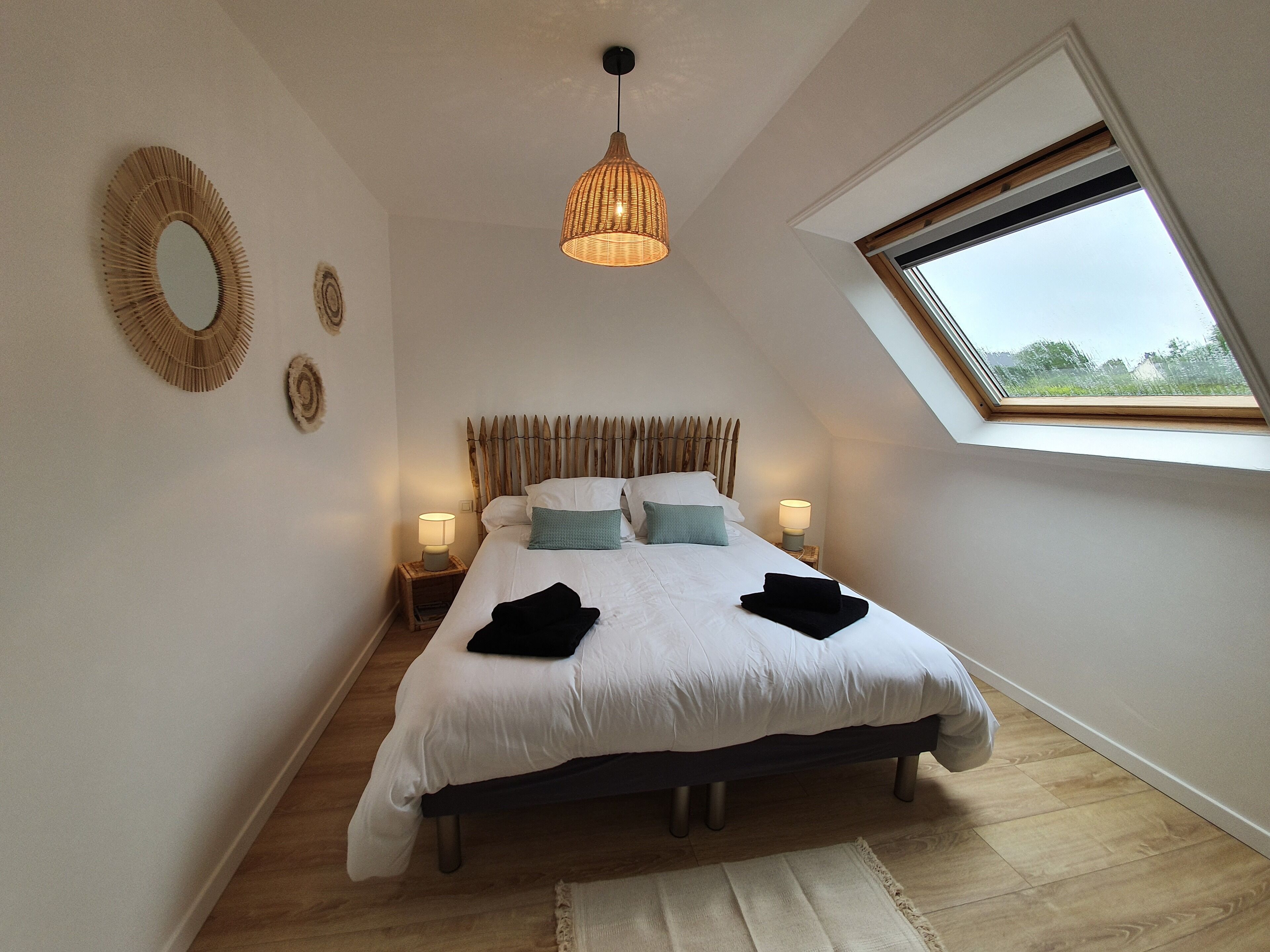 A bedroom with a large bed, two bedside tables with lamps, a skylight, and a circular mirror on the wall.