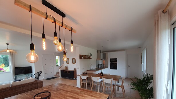 Una cocina moderna con una isla de madera, luces colgantes y un comedor con sillas.