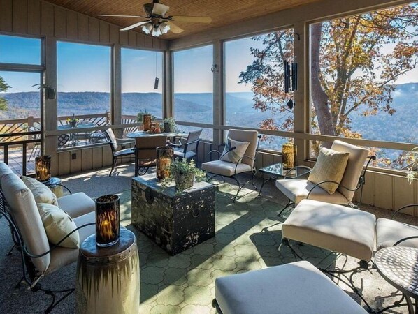 Relax in a serene outdoor space with a panoramic view of the surrounding hills and trees, surrounded by comfortable seating and a ceiling fan.