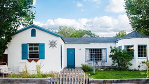 Ein weißes Gebäude mit blauen Fensterläden und einer blauen Tür, ein Holzzaun mit der Nummer 650 und ein kleiner Garten.